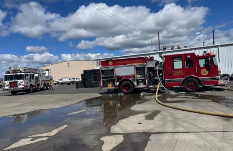 Fire crews stage apparatus outside the warehouse as suppression efforts continue to prevent the fire from spreading.