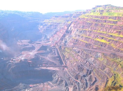 High-angle view of a vast, terraced open-pit iron ore mine in Brazil with red soil and long covered conveyor belts traveling up the steep pit walls.