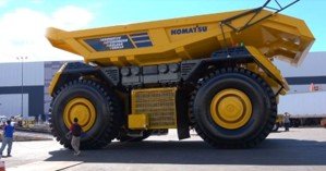 A massive yellow Komatsu cabless autonomous haul truck parked on an apron, completely lacking a driver’s cabin above its front wheels.