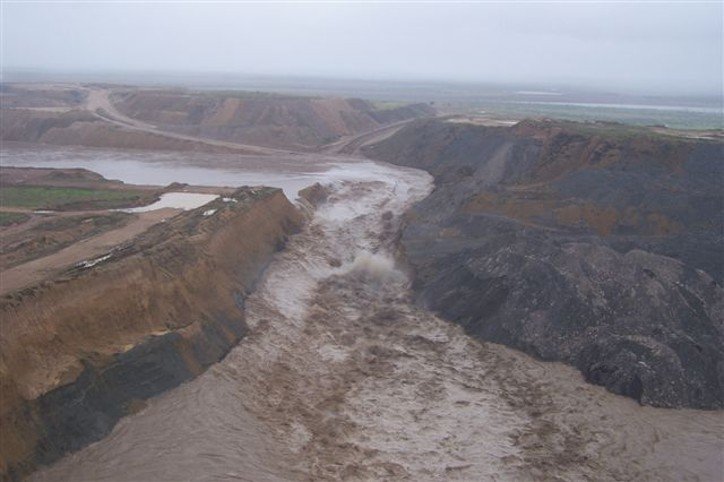Aerial view of muddy floodwaters rushing through a breached embankment into a large surface coal mine pit in Queensland, Australia.