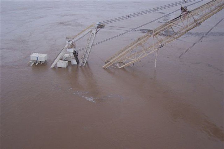 High-angle view of a giant mining dragline partially submerged in deep, murky brown floodwater, with only its upper housing and boom visible.