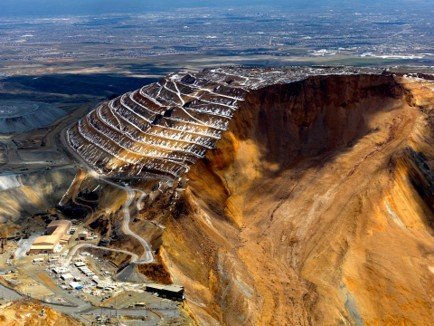 Aerial view of a massive landslide at the Bingham Canyon open-pit mine, showing a vast slope failure where a huge section of terraced rock wall collapsed into the pit toward a maintenance complex below.