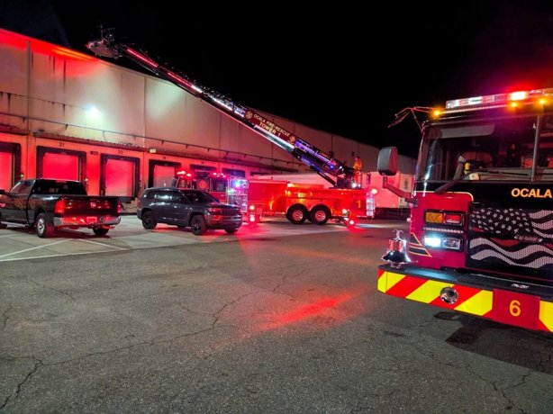 Firetrucks outside warehouse with lights on and a ladder extended